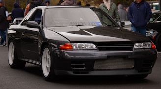 a black car driving down a street next to a crowd of people