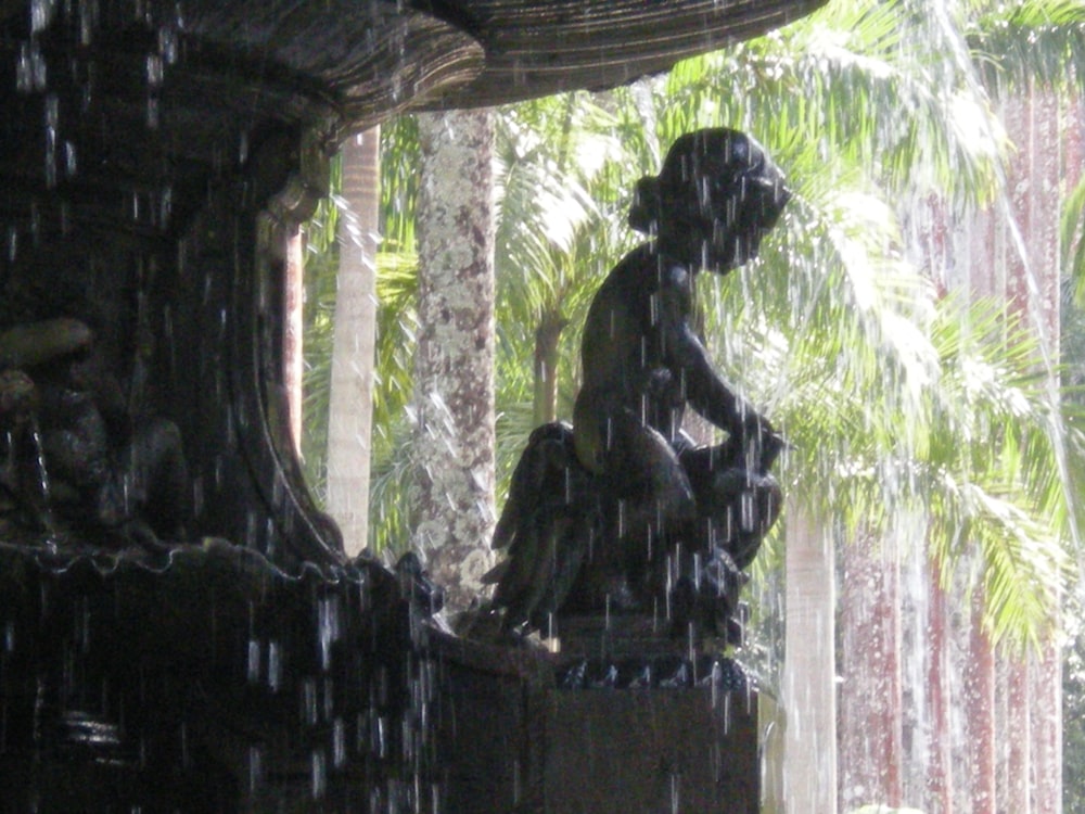 a statue of a person sitting on a bench in the rain