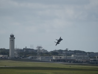 a plane flying over a field with a tower in the background