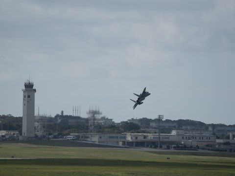 a plane flying over a field with a tower in the background