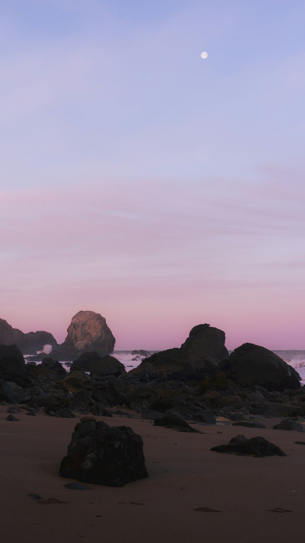 a beach with rocks and a full moon in the sky