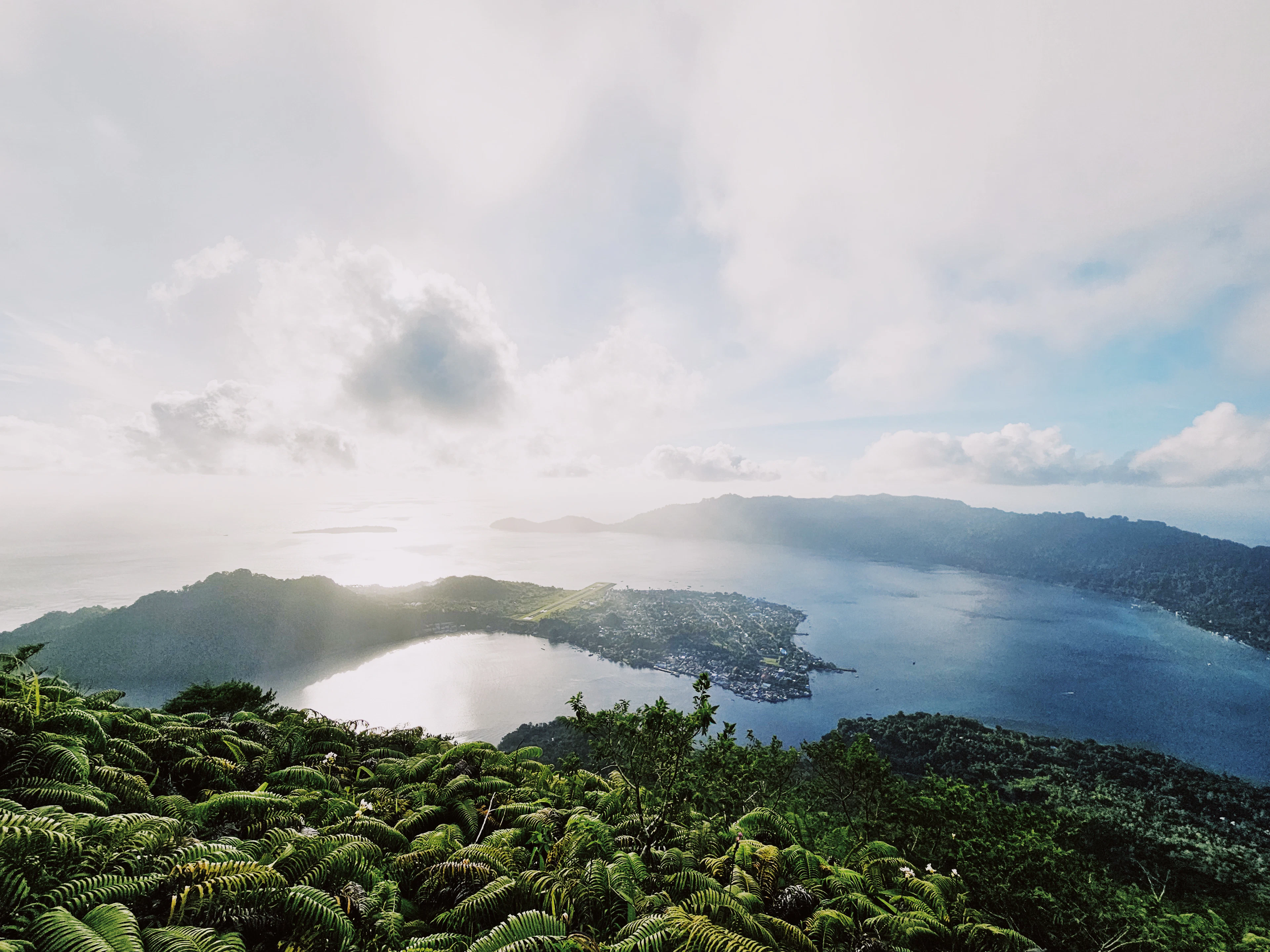 The landscape of Banda Neira: green shores, calm water and a cloudy sky