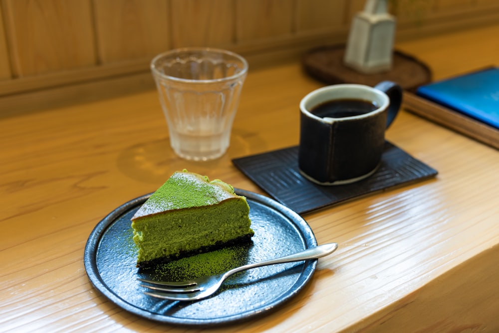 a piece of green cake on a plate next to a cup of coffee