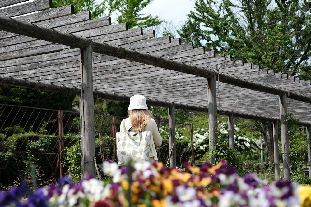 a woman in a white hat walking through a garden