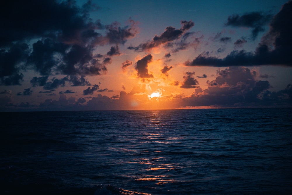 the sun is setting over the ocean on a cloudy day