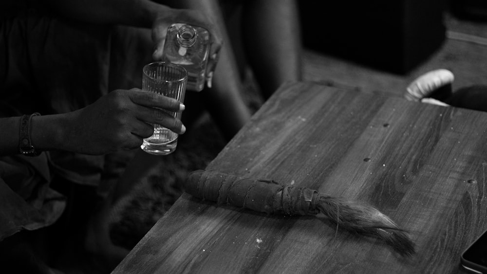 a person holding a glass and a knife on a wooden table