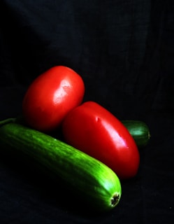 two tomatoes and a cucumber on a black background