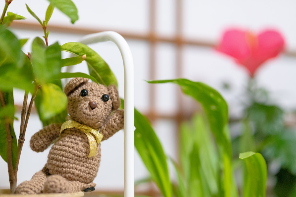 a crocheted teddy bear sitting next to a potted plant