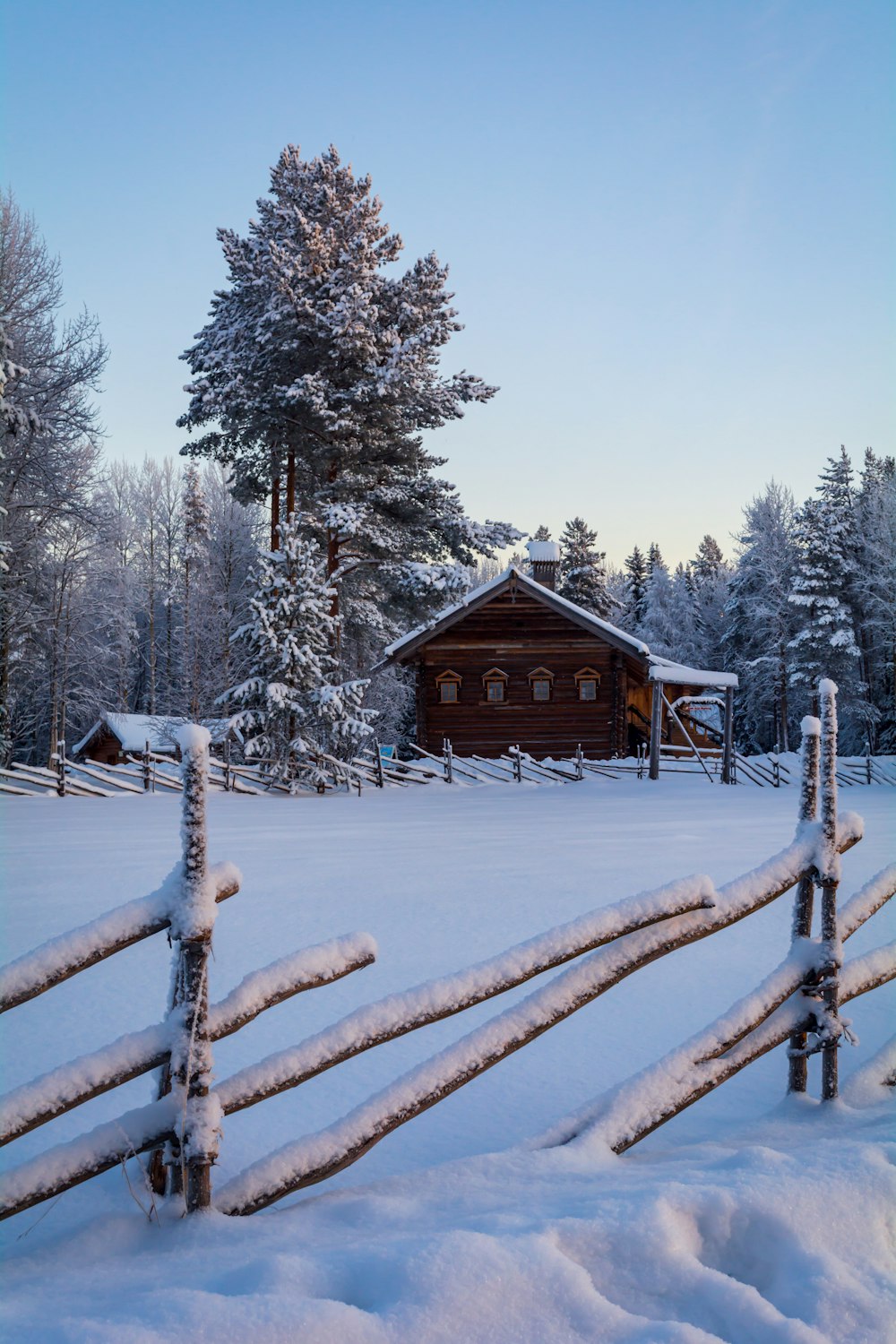 a snow covered field with a fence and a cabin in the background