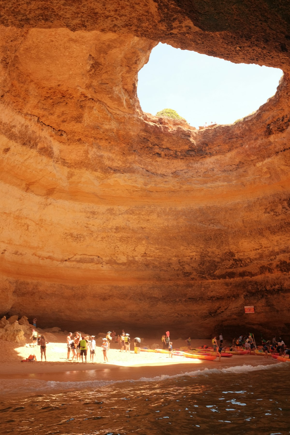 Visitors inside Benagil Cave standing on the beach with golden cliffs surrounding them