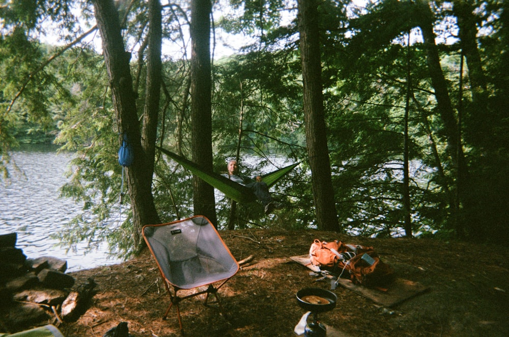 a camping area with a chair and a hammock next to a lake