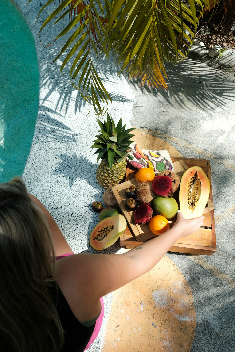 a woman holding a tray of fruit next to a pool