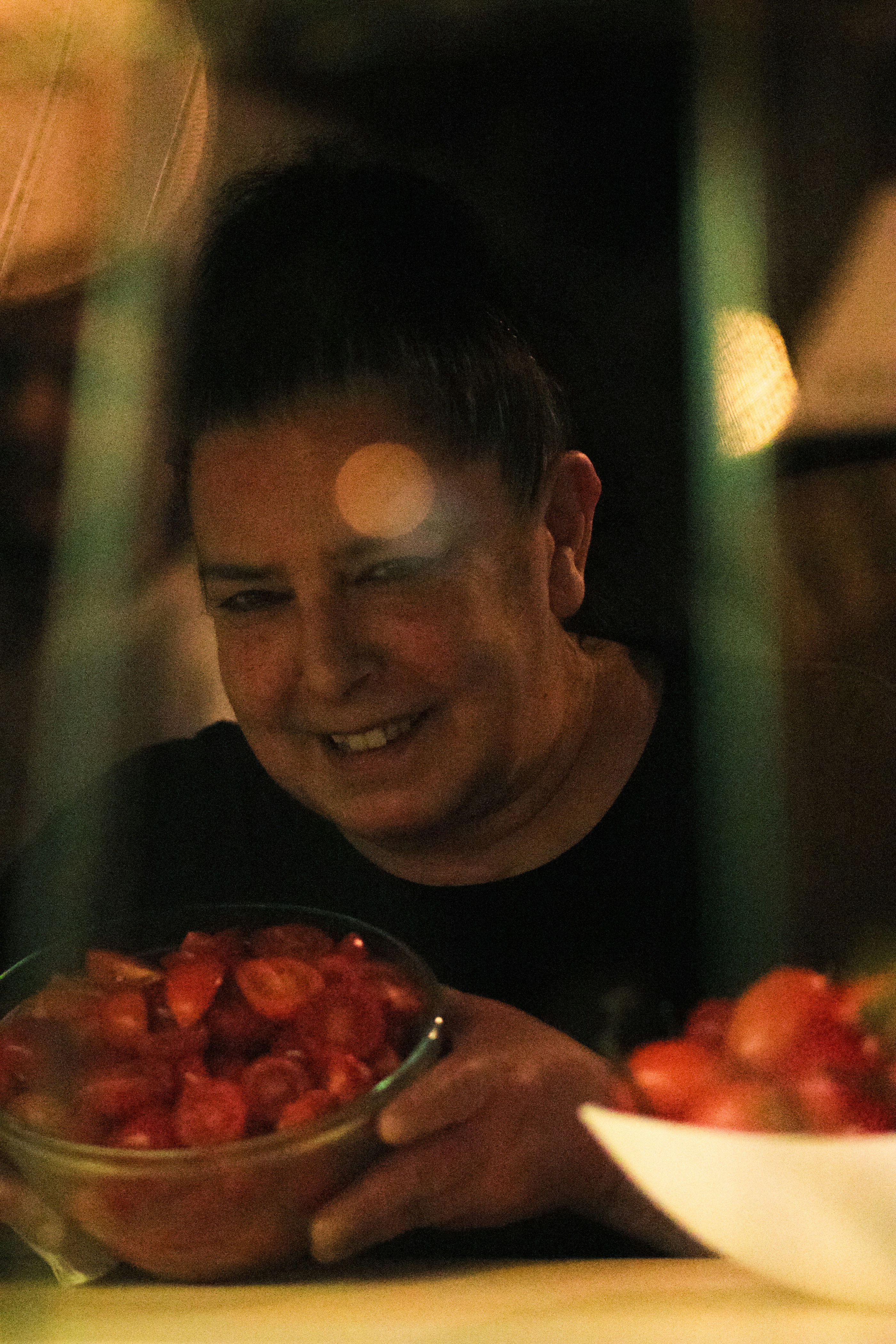 a man smiles as he holds a bowl of strawberries