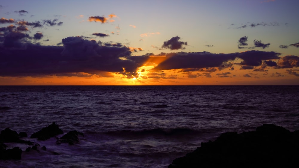 a sunset over a body of water with rocks in the foreground