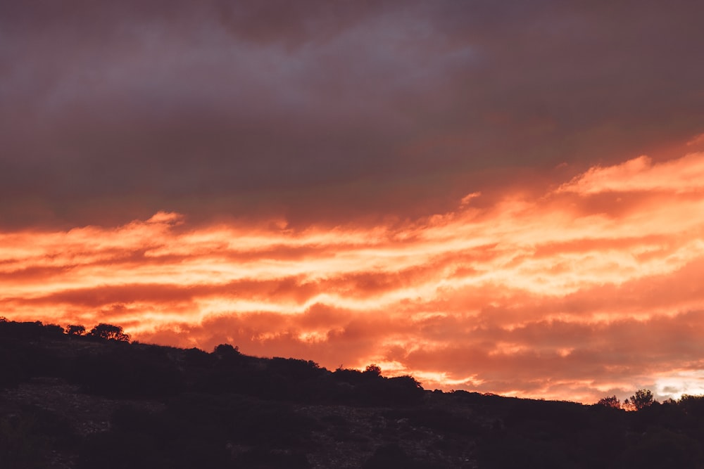 a red sky with clouds over a hill