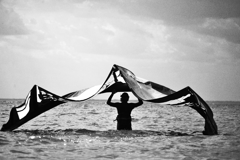 a man standing in the ocean holding a large kite