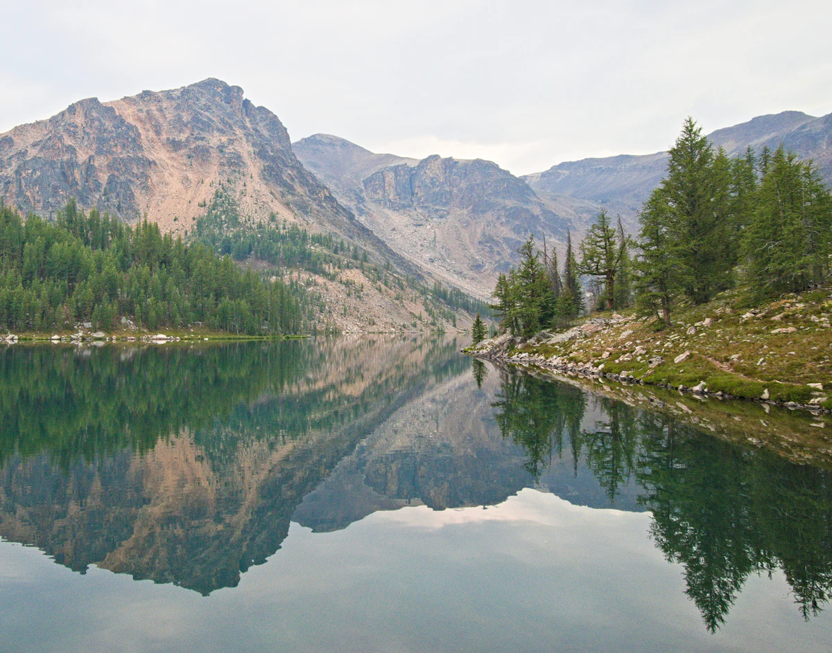A still lake in Cathedral Provincial Park reflecting a rocky peak, with conifers on the shore