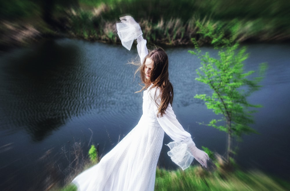 a woman in a white dress is standing by a lake