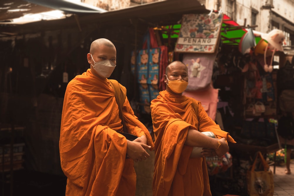 two monks in orange robes with masks on
