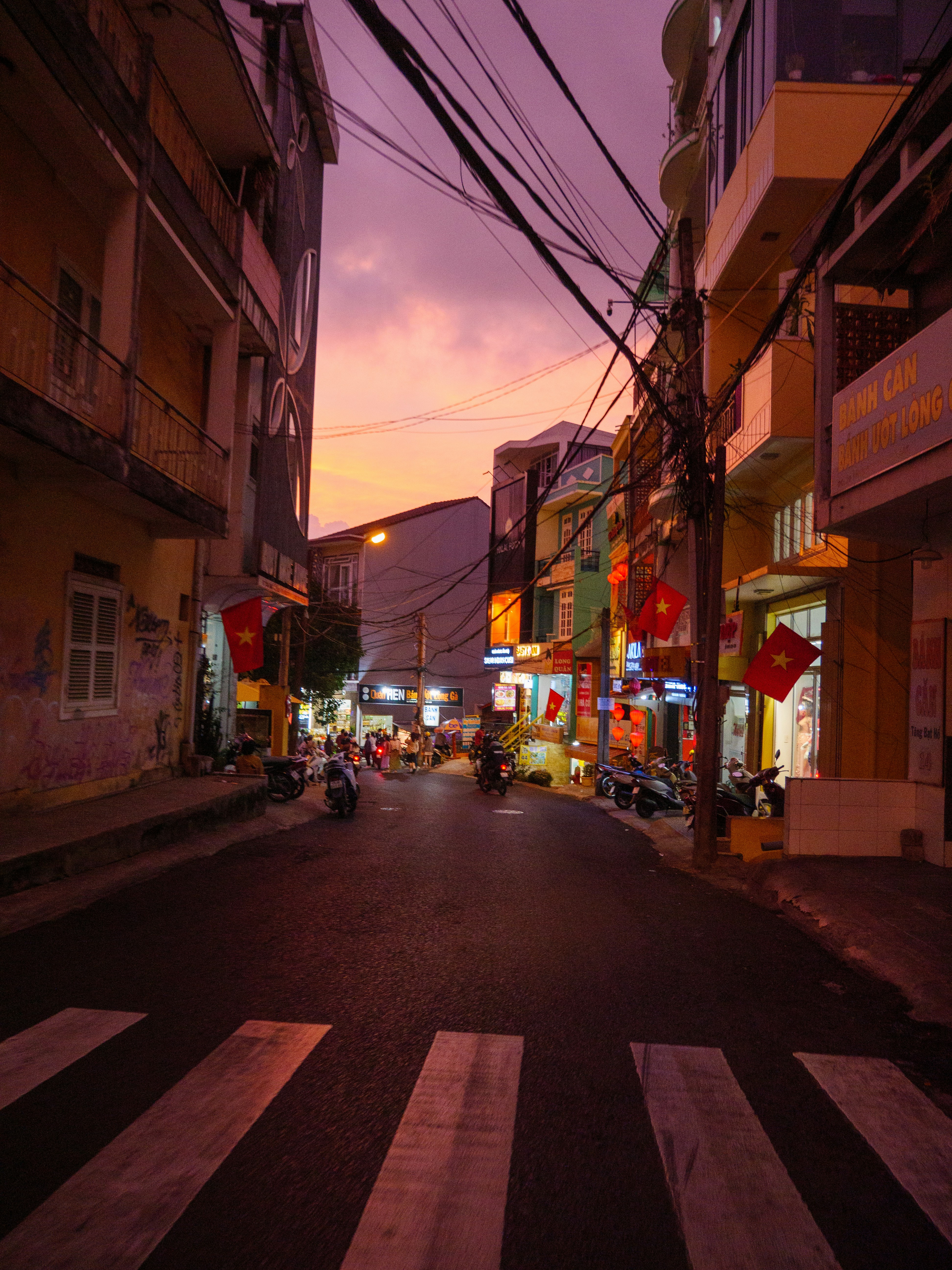 A city street at dusk with a few cars parked on the side of the road ...