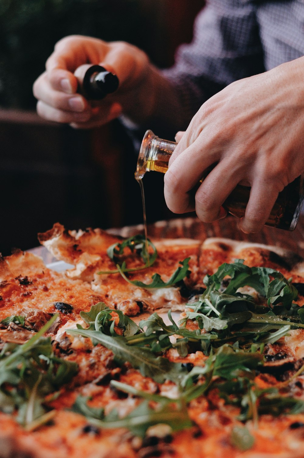 a person pouring olive oil on a pizza