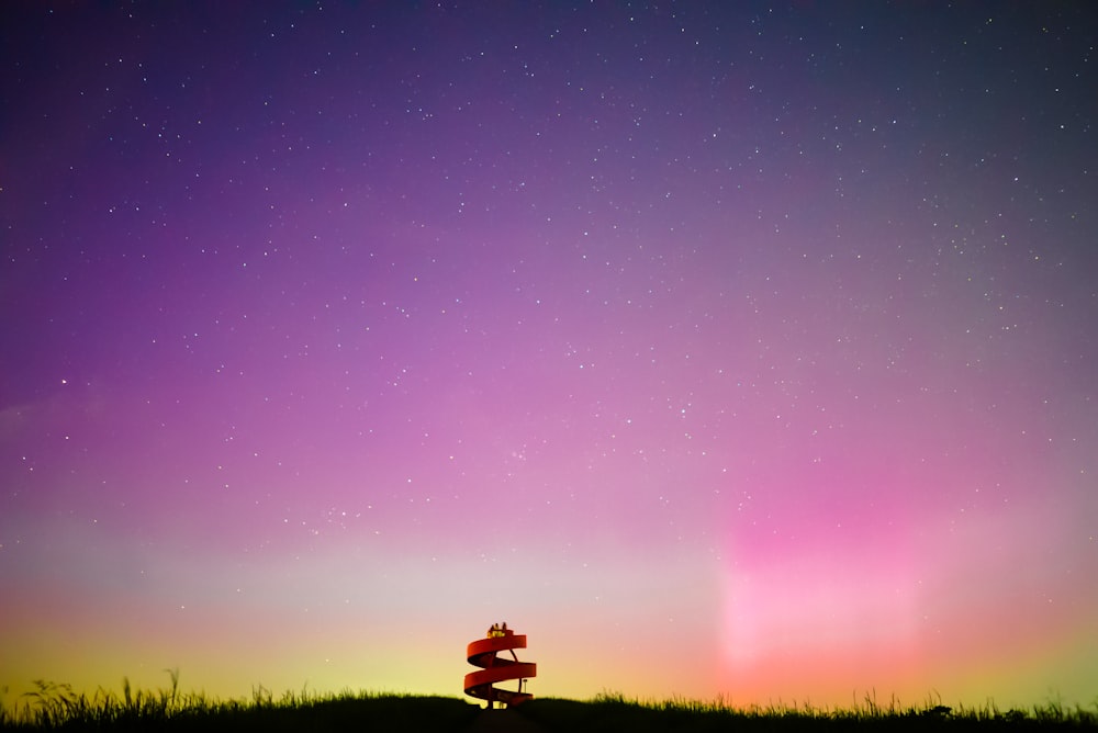 a bench sitting on top of a grass covered hill under a purple sky