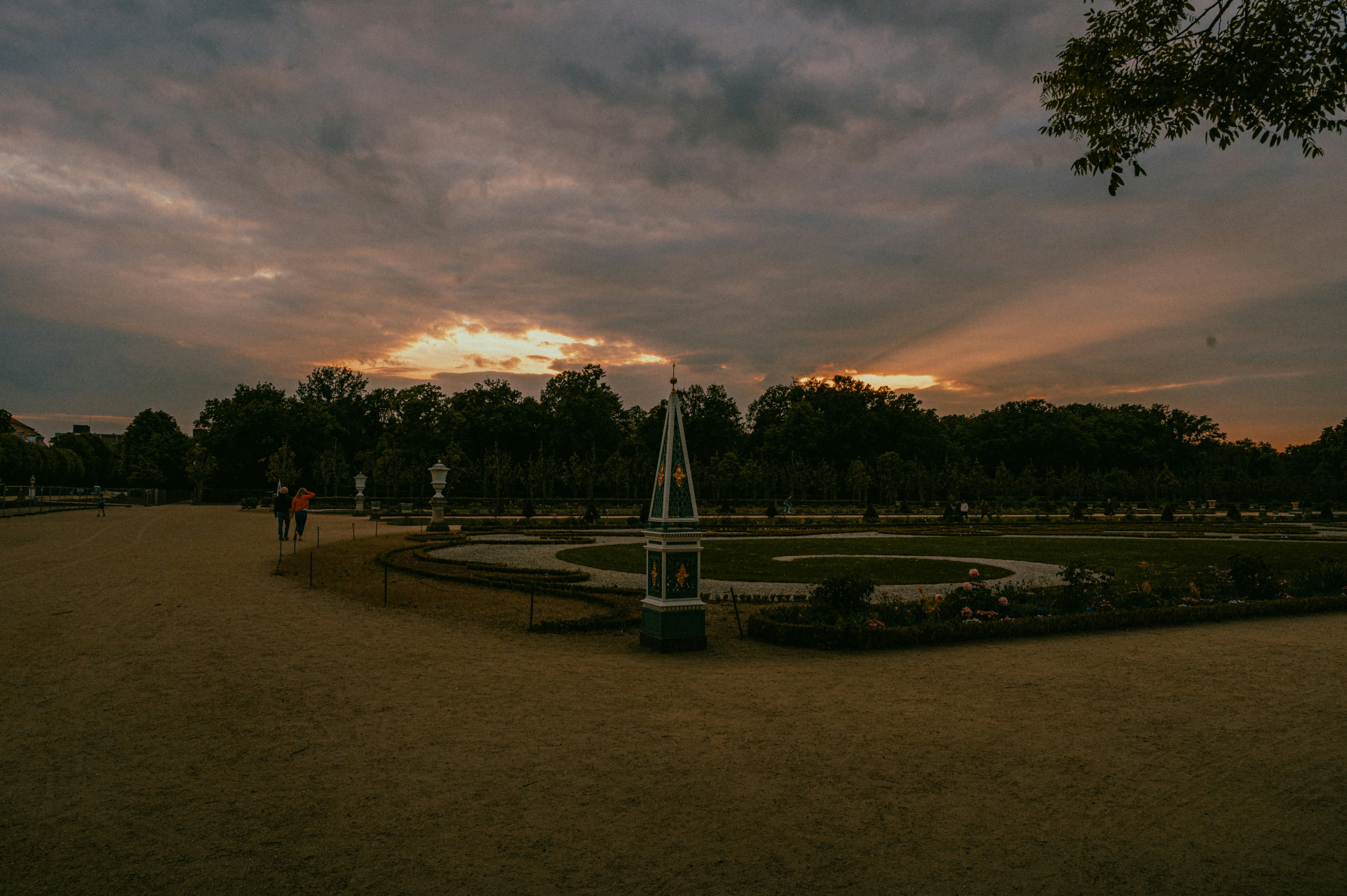 ein Uhrenturm in einem Park mit einem Sonnenuntergang im Hintergrund
