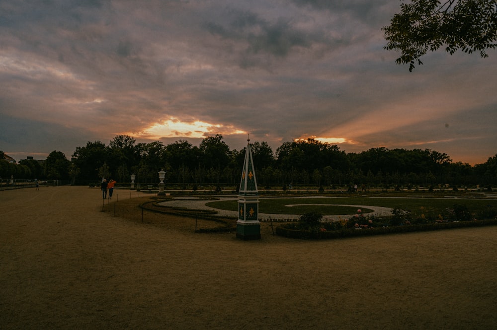 una torre de reloj en un parque con una puesta de sol de fondo