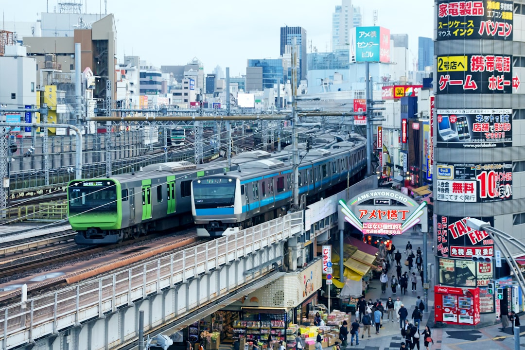 a green train traveling down train tracks next to tall buildings, Two metro trains are running simultaneously on the rai