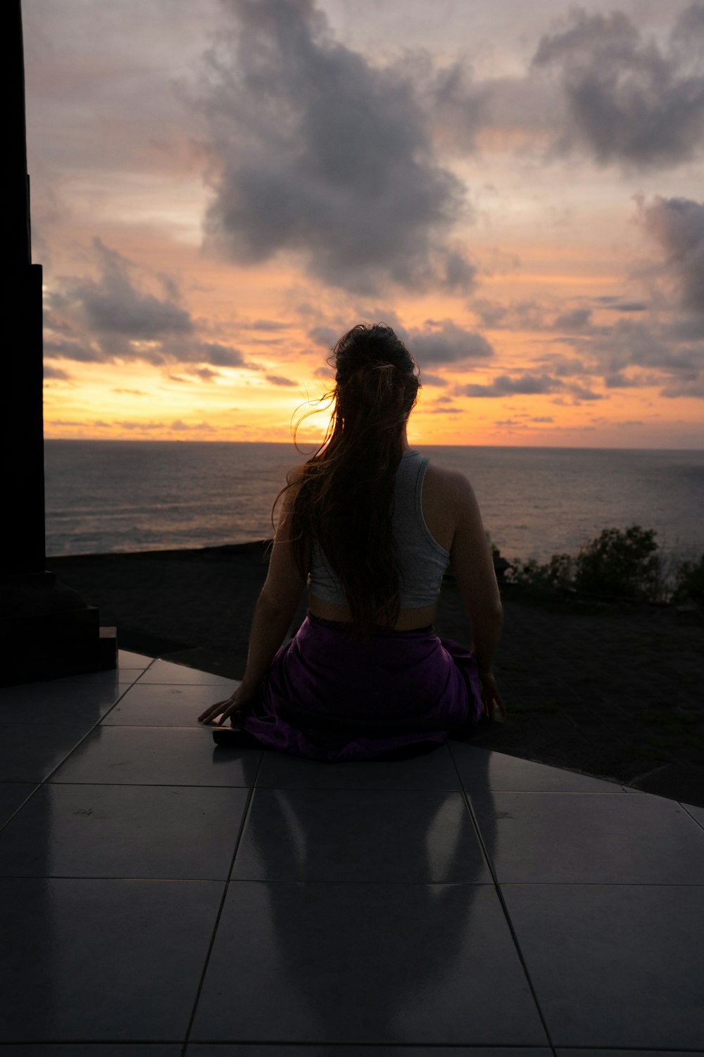 a woman sitting on the ground in front of a sunset