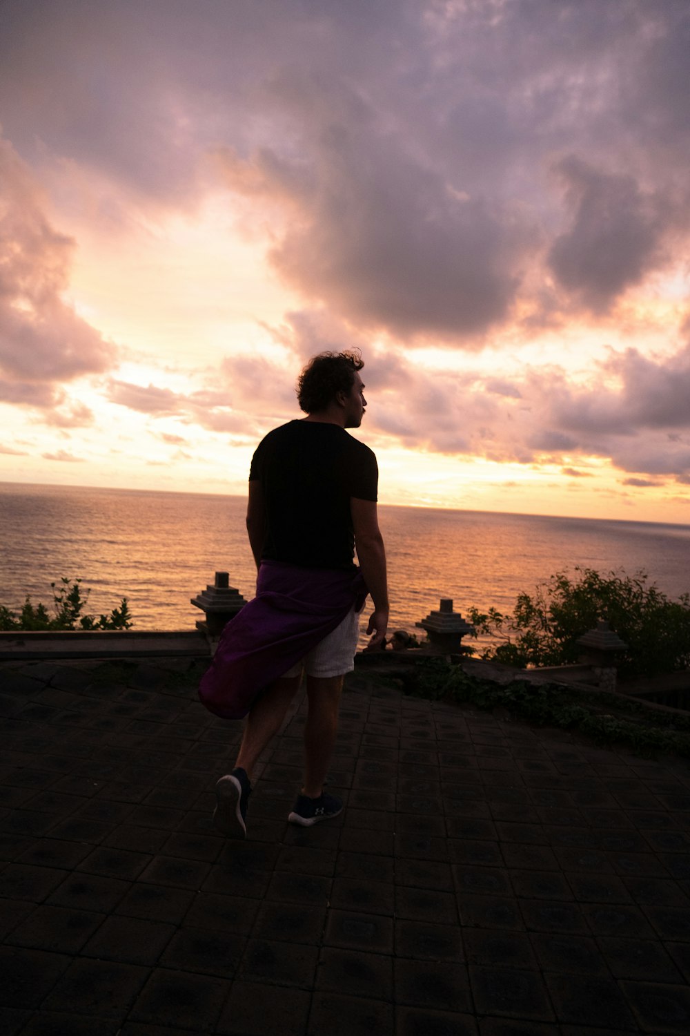 a man standing on top of a brick walkway next to the ocean