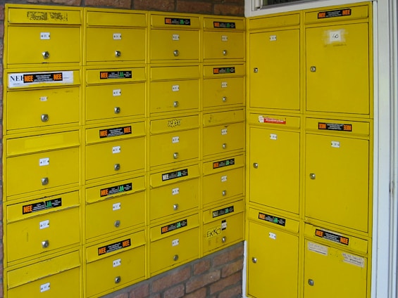 a bunch of yellow mail boxes sitting next to a brick wall