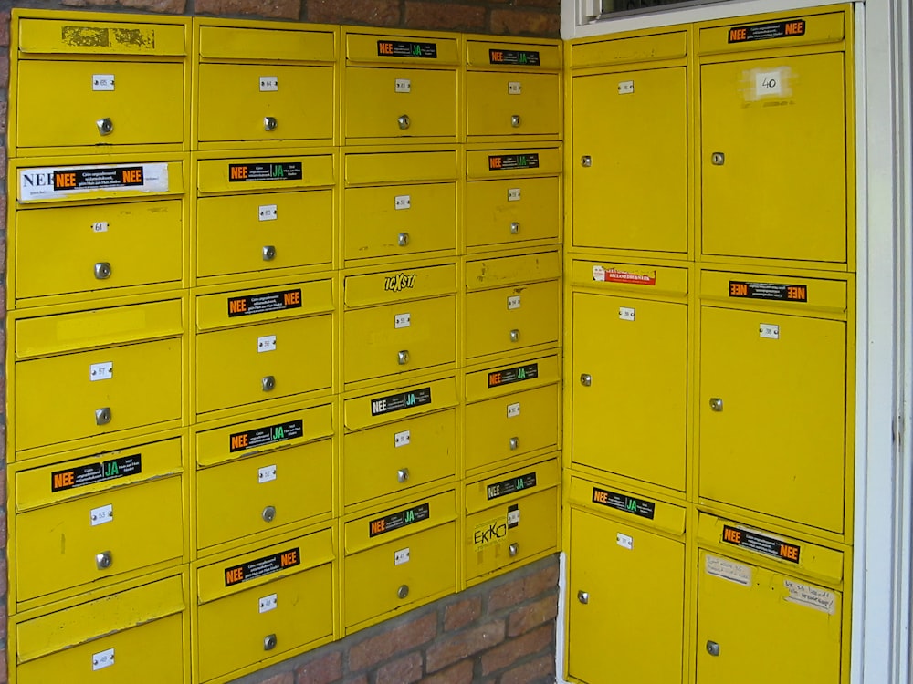 a bunch of yellow mail boxes sitting next to a brick wall