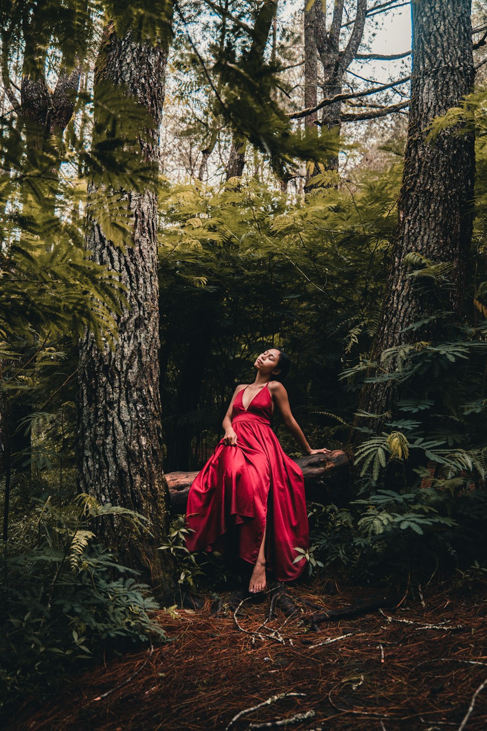 a woman in a red dress standing in a forest
