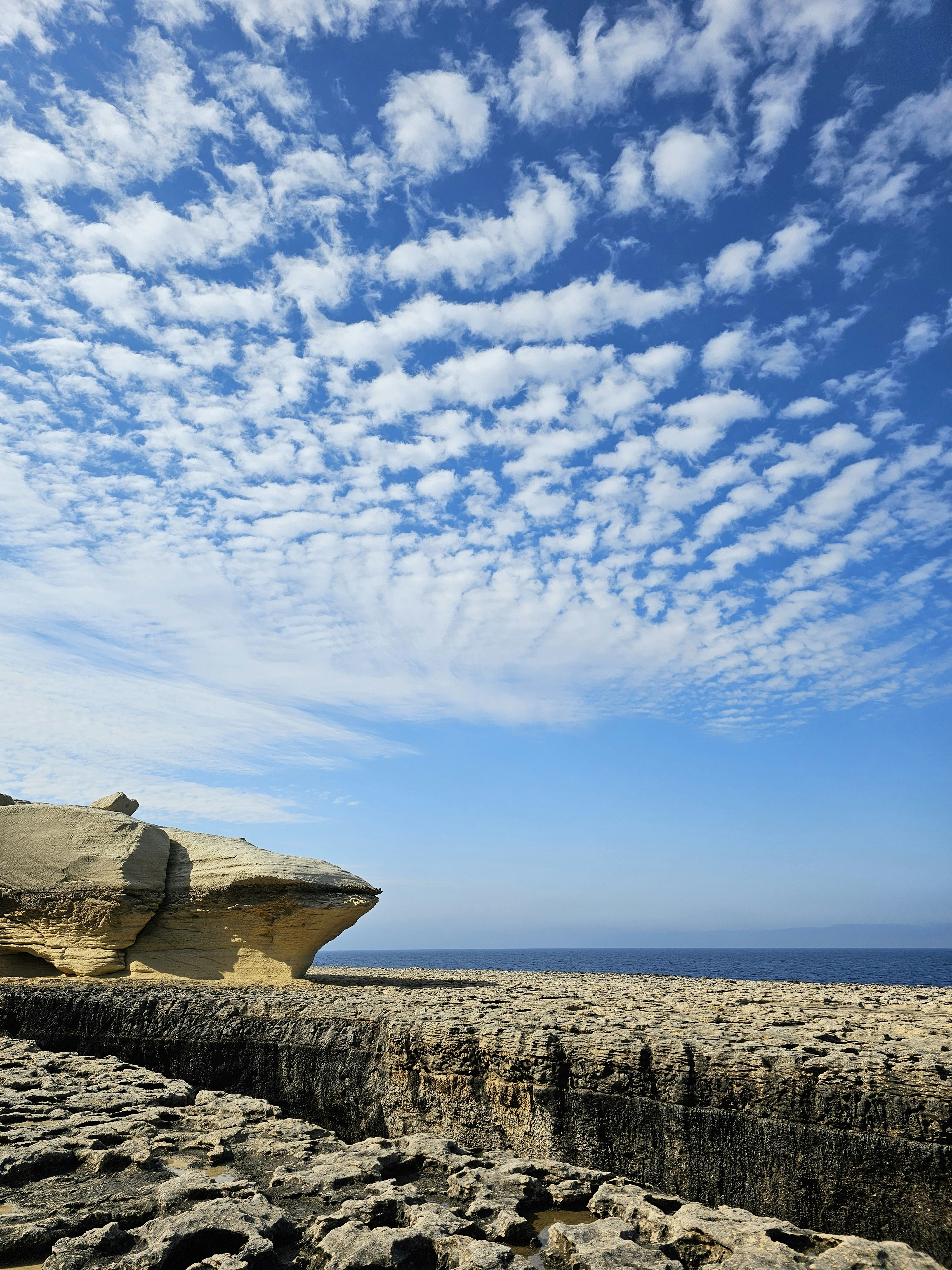 Dramatic rocky coastal cliffs with lighthouse on top, bright blue sky, vast ocean below