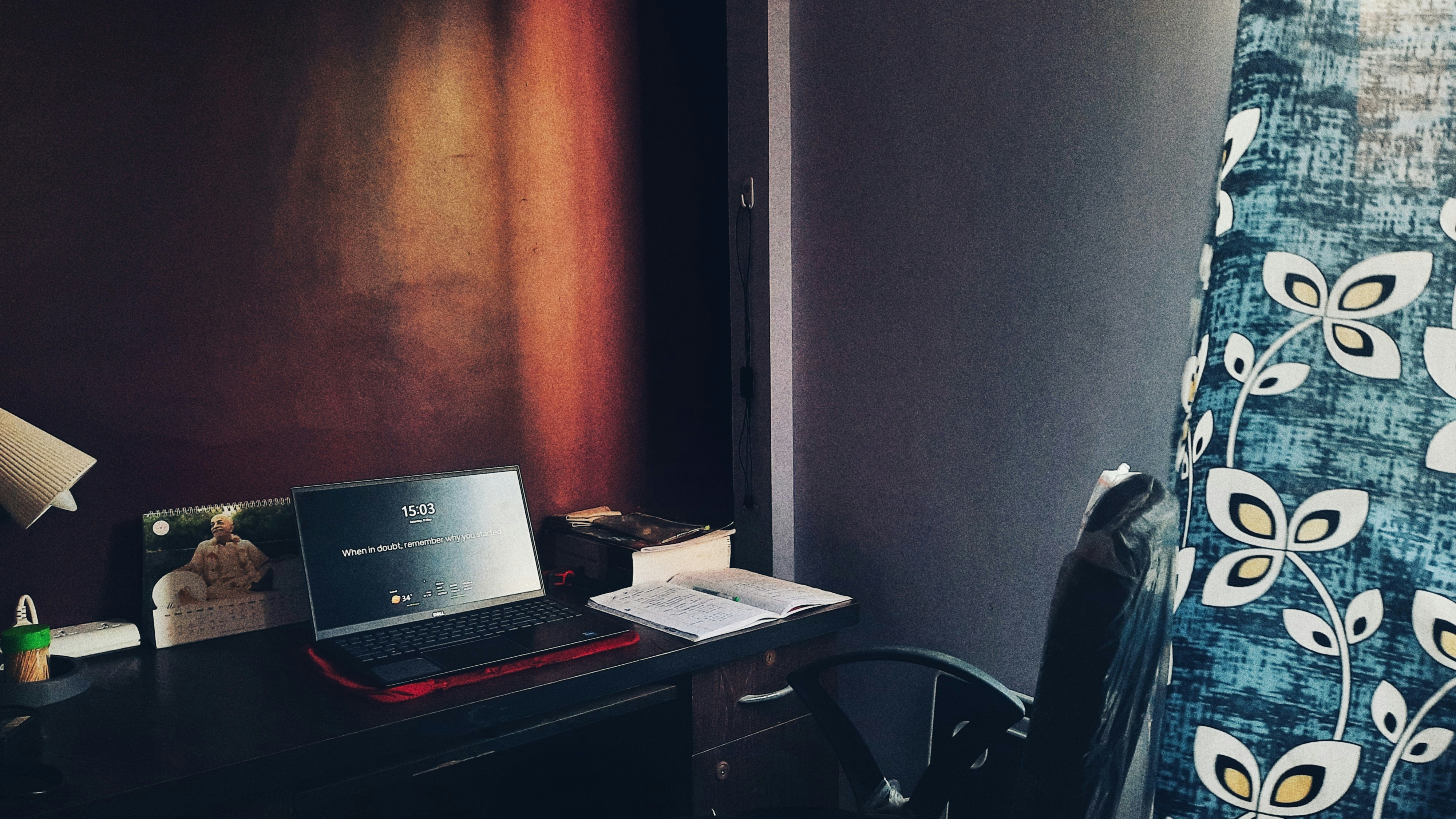 Calendar with handwritten notes on dark desk, scattered pens and notebooks, focused desk lamp
