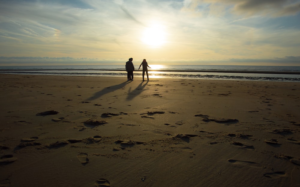 two people standing on a beach at sunset