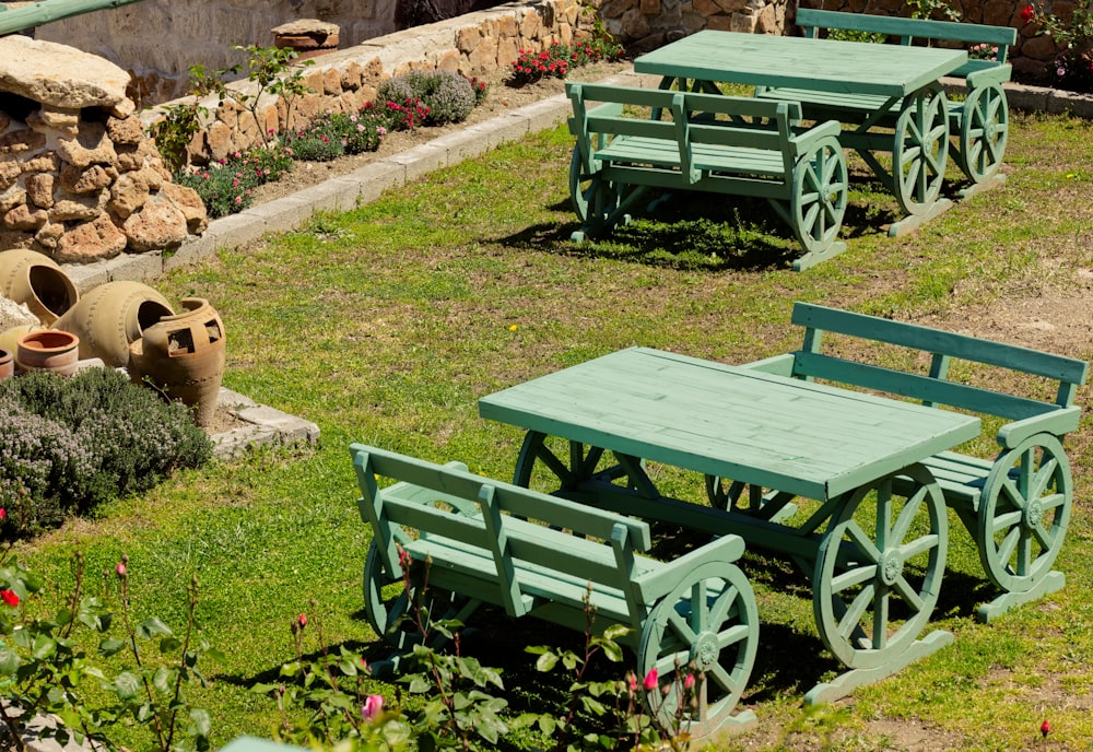 eine Gruppe von grünen Tischen und Bänken in einem Garten