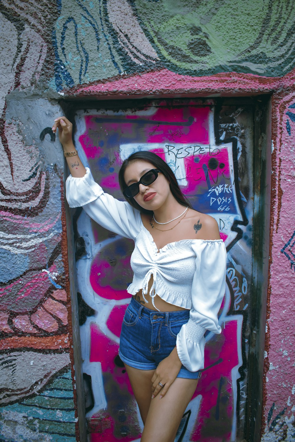 a woman in a white top and denim shorts posing in front of a graffiti wall