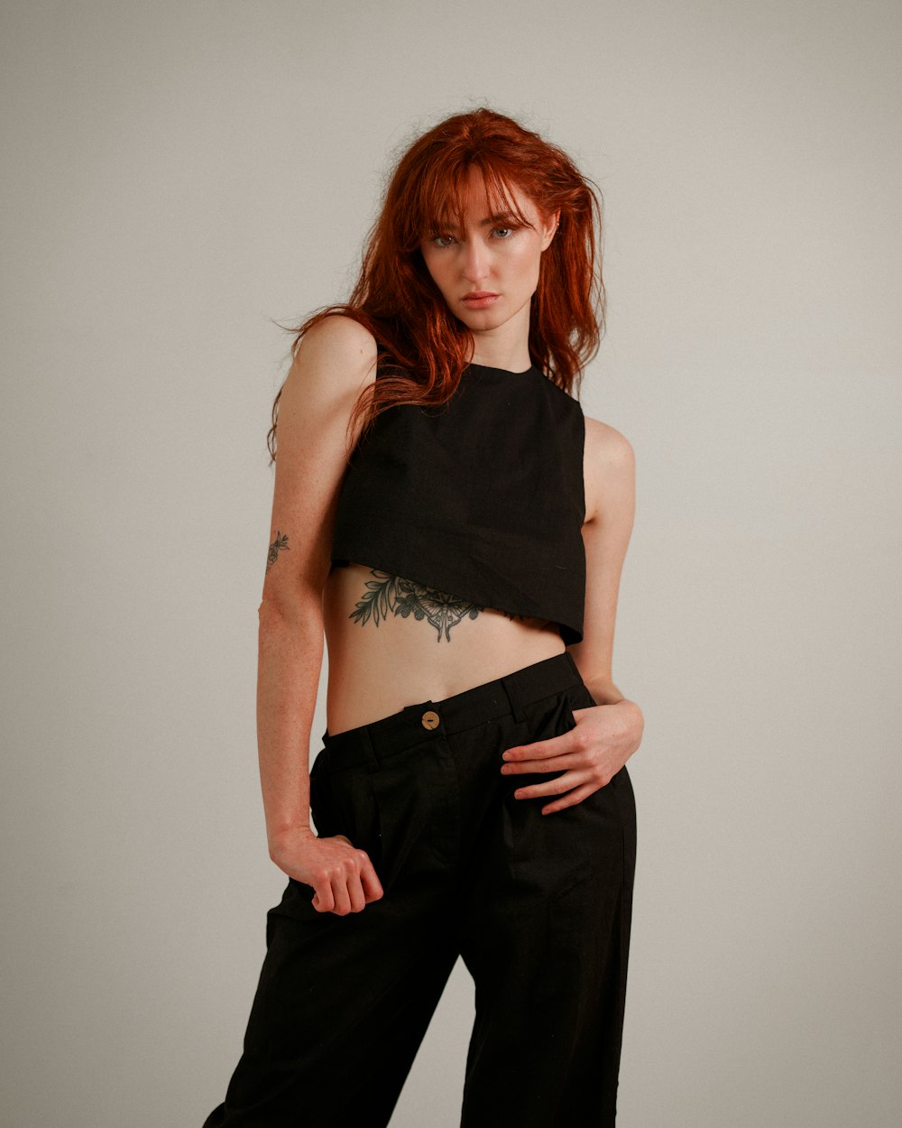 a woman with red hair wearing black pants and a crop top