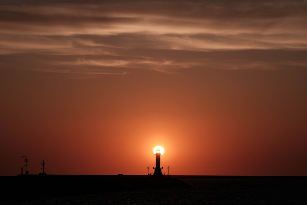 the sun is setting behind a lighthouse on the ocean