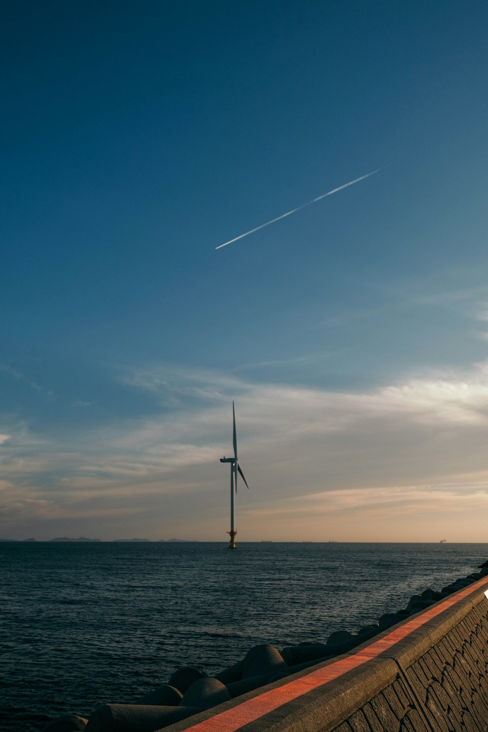 a wind turbine in the distance with a body of water in the foreground