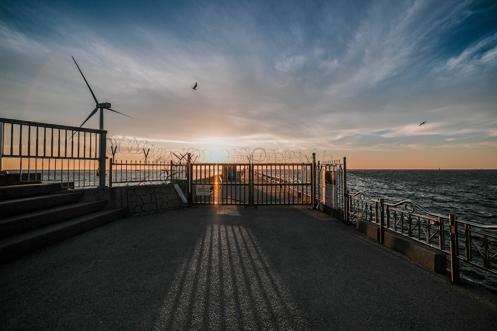 the sun is setting over the ocean with a windmill in the distance