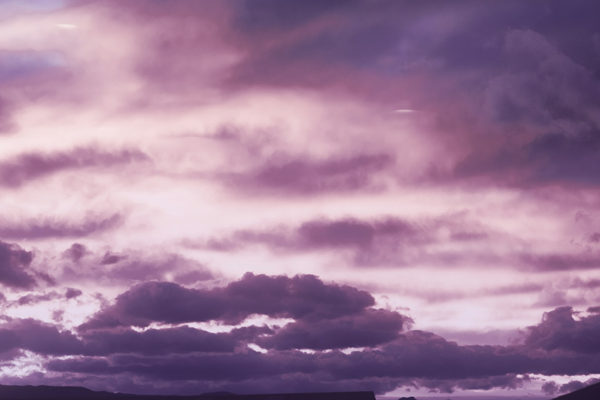 a plane flying through a cloudy sky with mountains in the background