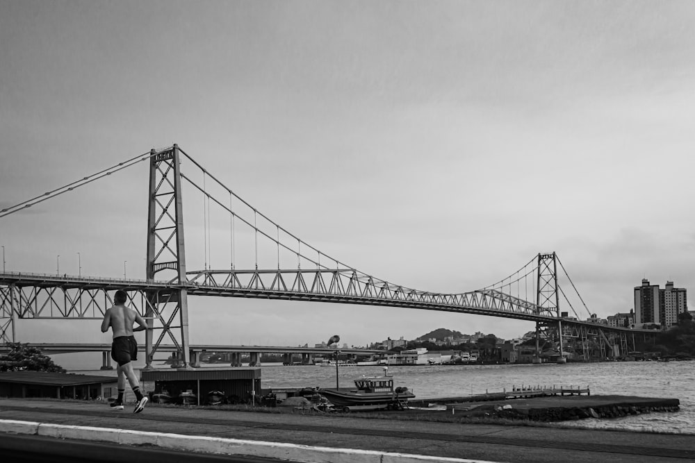 a black and white photo of a man walking across a bridge