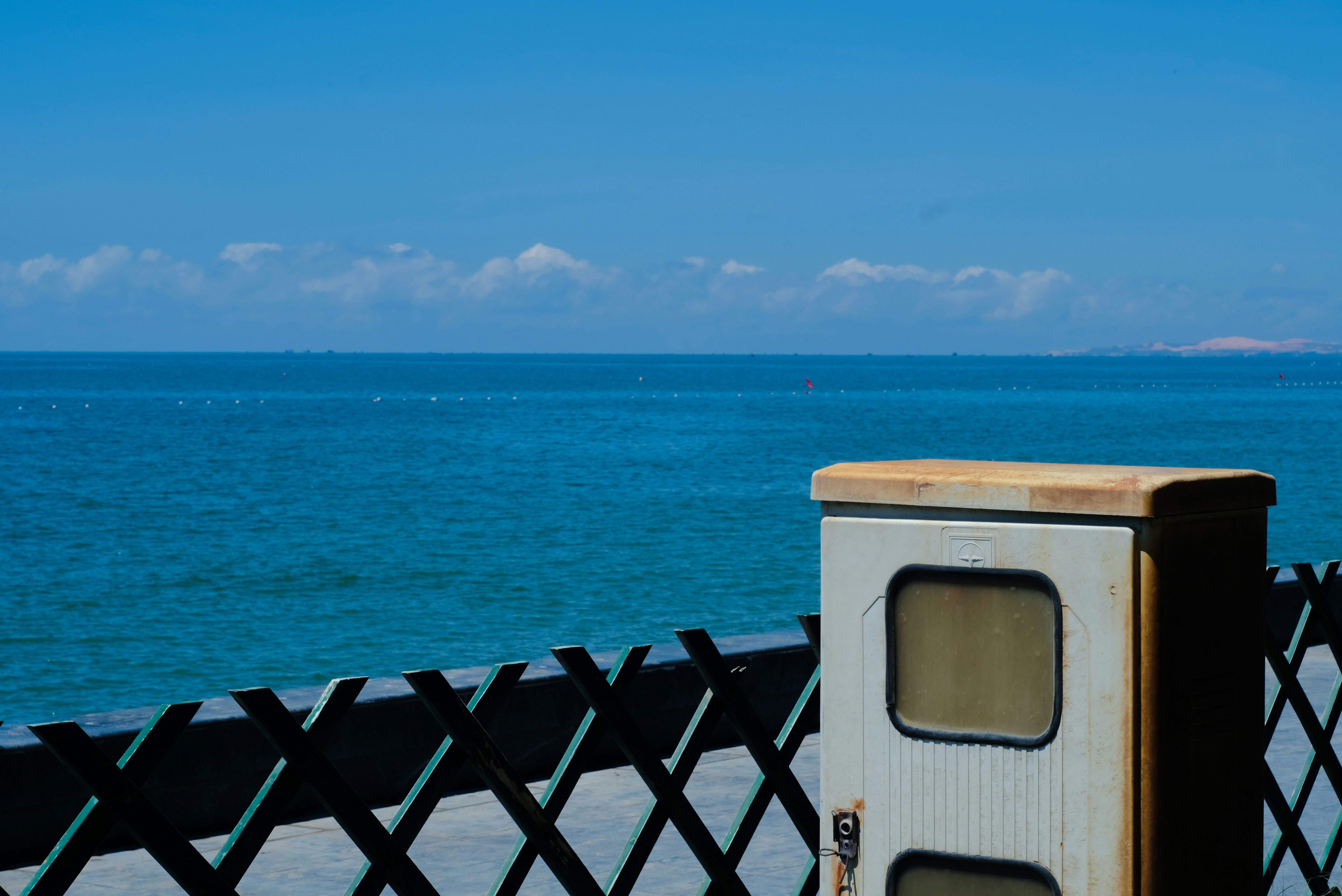 a box sitting on the side of a fence next to the ocean