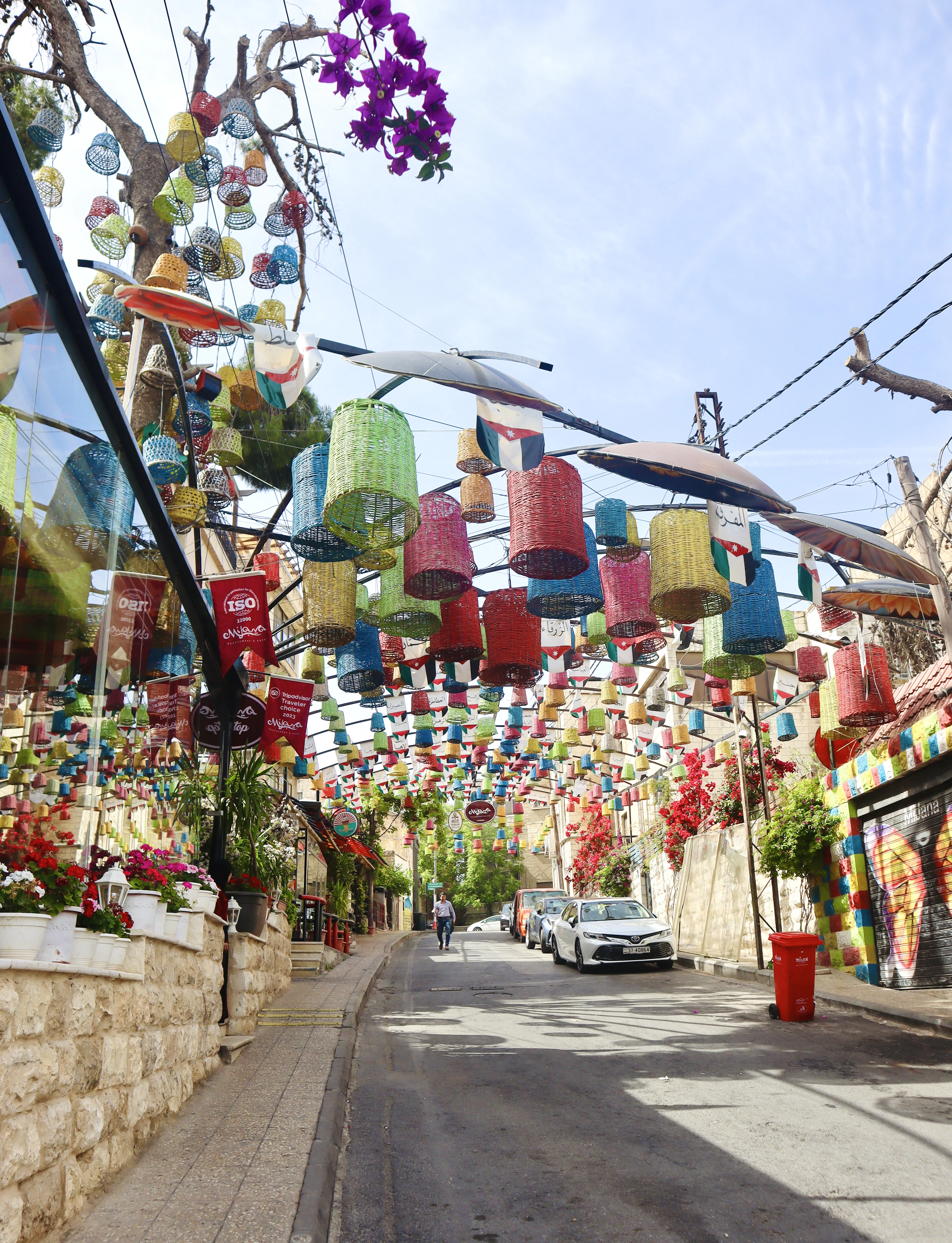 Colorful woven lantern decorations hang over a sloping café-lined street on Amman's Rainbow Street.