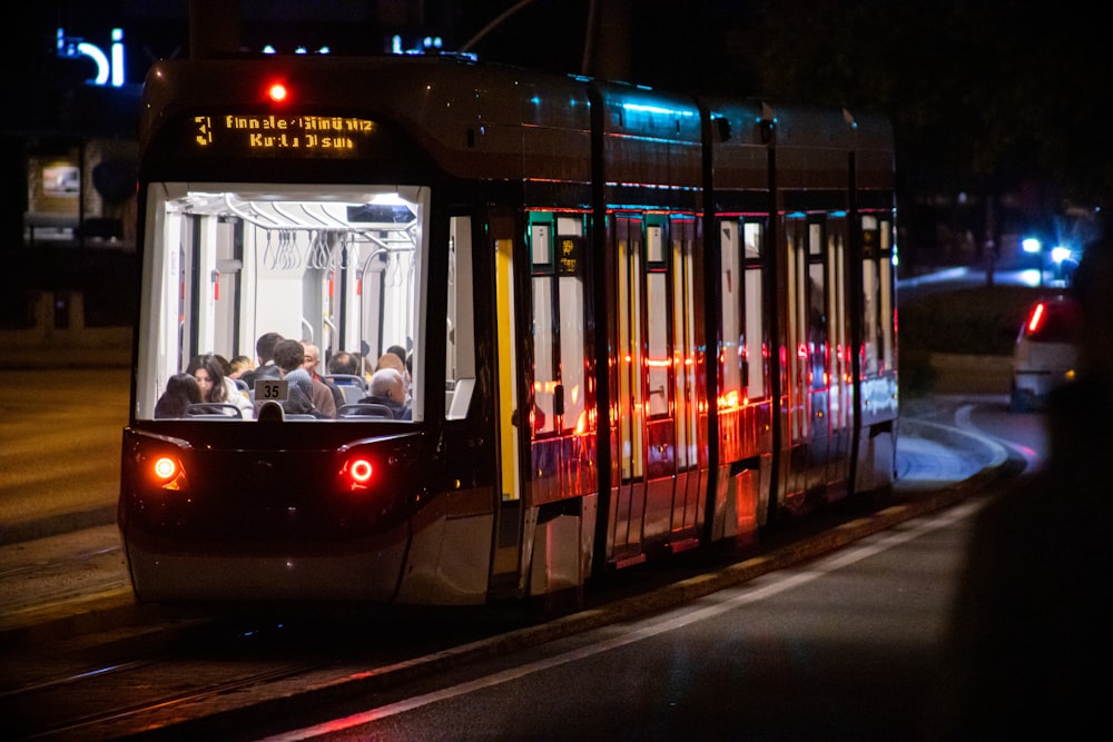 a trolley car with people inside traveling down the street at night
