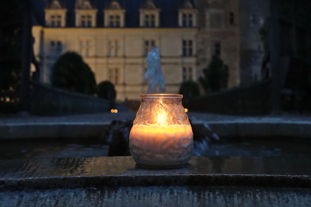 a lit candle sitting on a ledge in front of a building