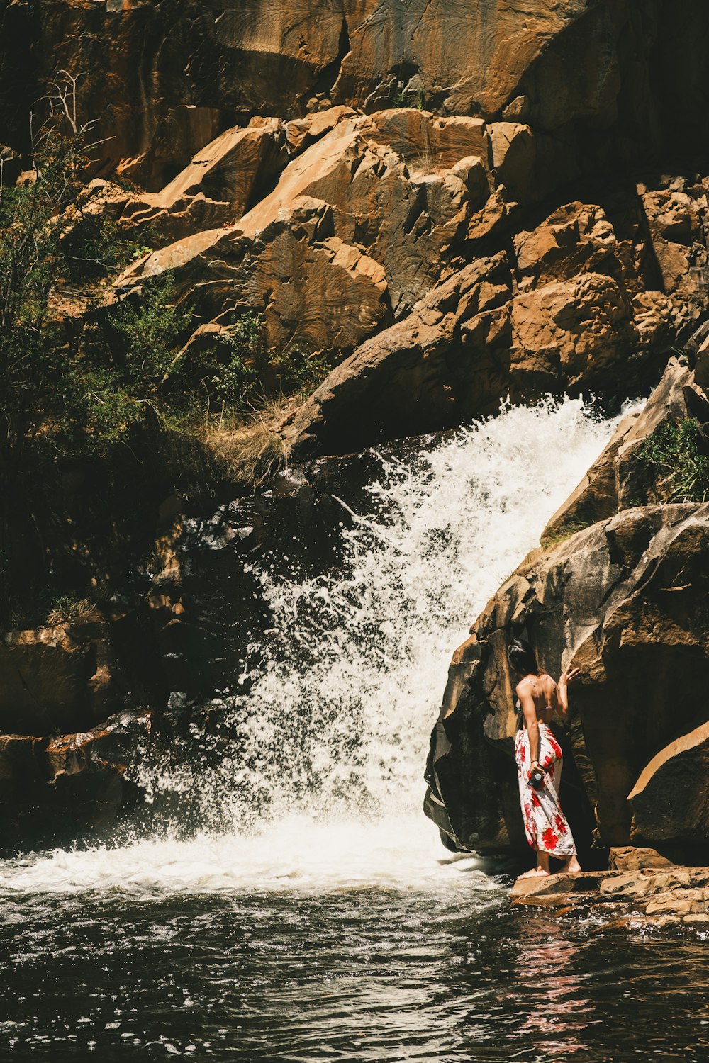 Un hombre parado sobre una roca junto a una cascada